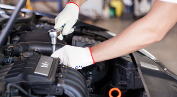 Mechanic wearing gloves tightens car engine bolt with socket wrench.